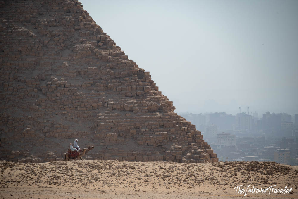 Camel rider beside the Pyramid of Menkaure at Giza, with hazy Cairo skyline beyond