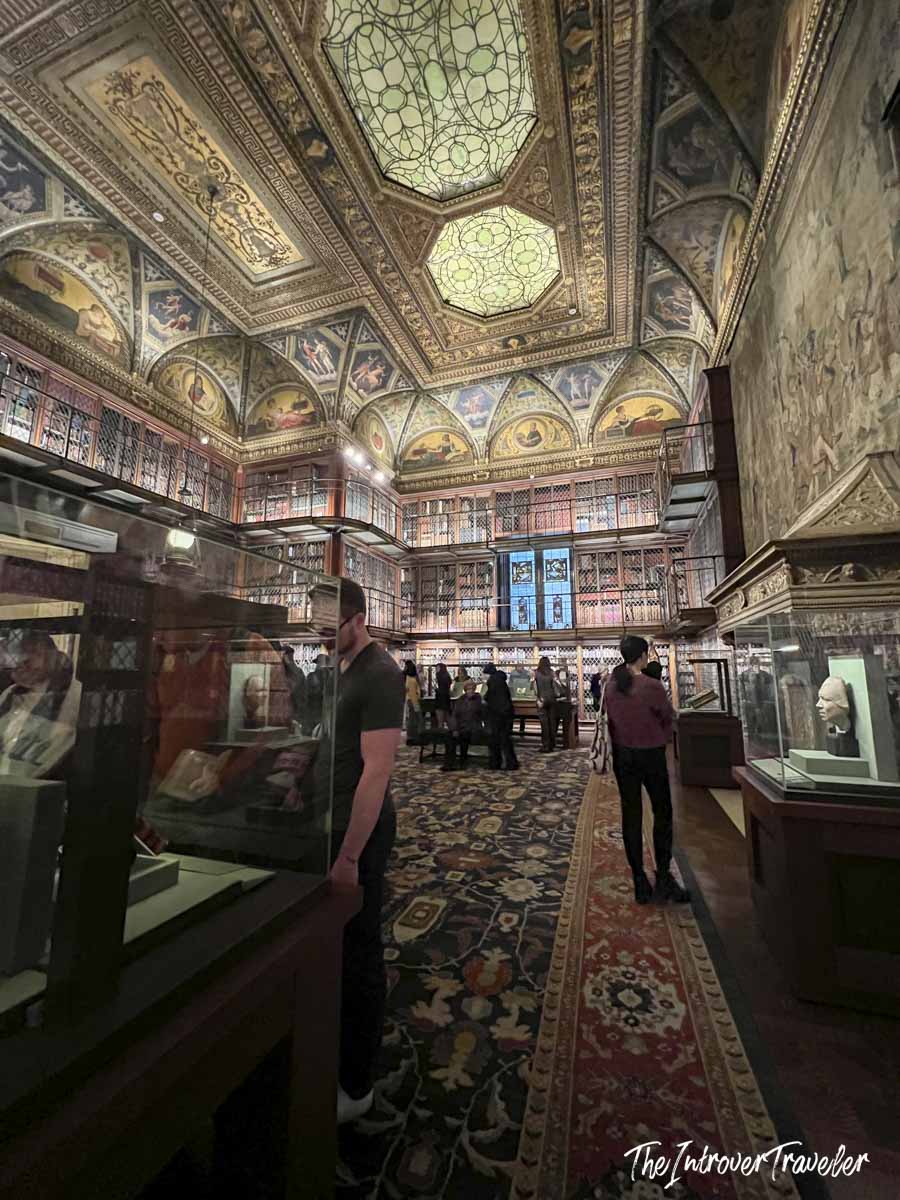 Visitors exploring the ornate East Room of the Morgan Library, with its painted vaulted ceiling and stained glass skylight