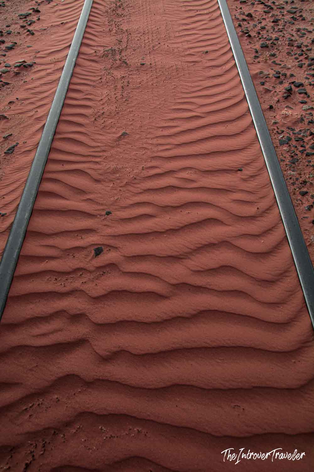 Red desert sand with wind ripples filling the railway tracks crossing Wadi Rum, Jordan