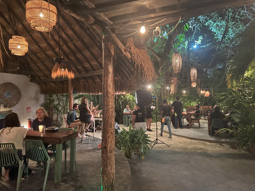 Kondesa Cozumel open-air dining room at night, with thatched roof, wicker pendant lights, and jungle greenery