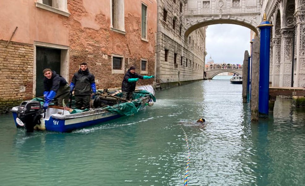 Workers on a boat near the Bridge of Sighs in Venice, assisting a diver cleaning the canal below