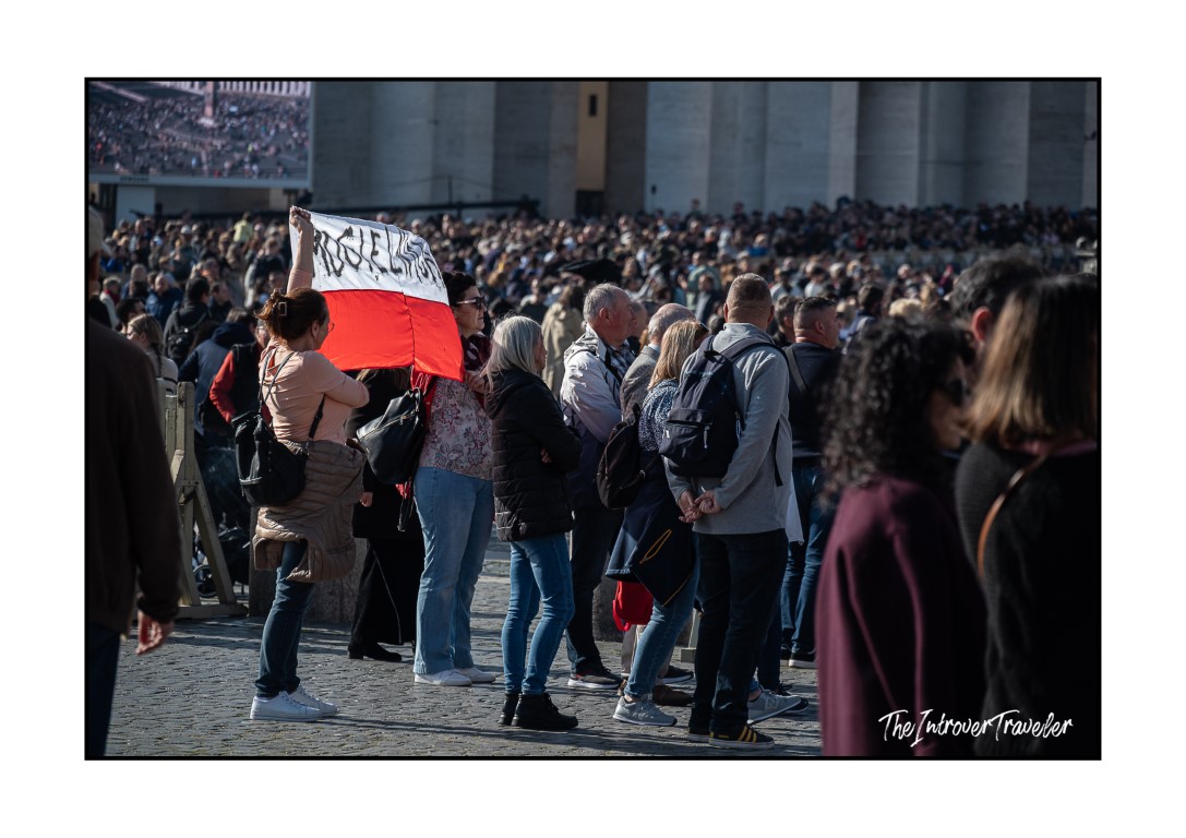 Polish pilgrim holding a red and white flag in the packed crowd at St. Peter's Square during the Papal Angelus
