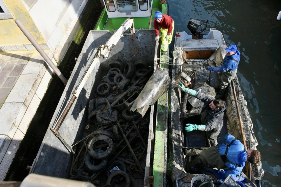 Workers dredging old tires and debris from a Venice canal during a waterway cleanup operation