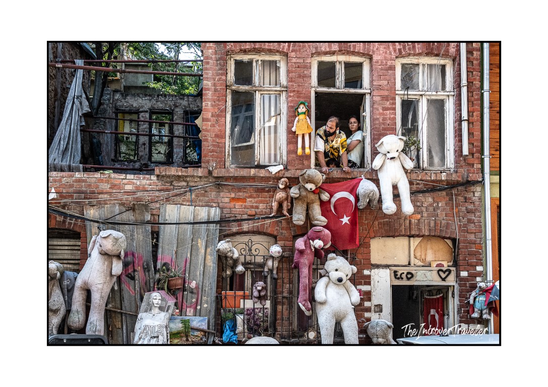 Eccentric Istanbul building covered in stuffed animals and a Turkish flag, with residents watching from window