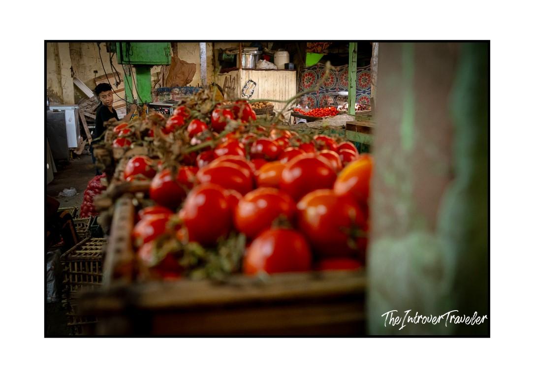 Vendor behind piles of fresh tomatoes at a bustling Egyptian market stall