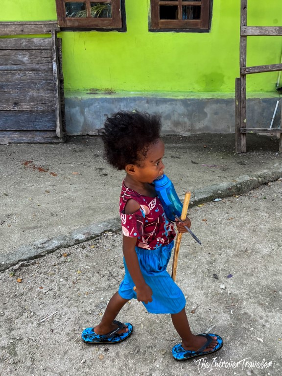 Young local child walking near a bright green village house in Raja Ampat, Indonesia