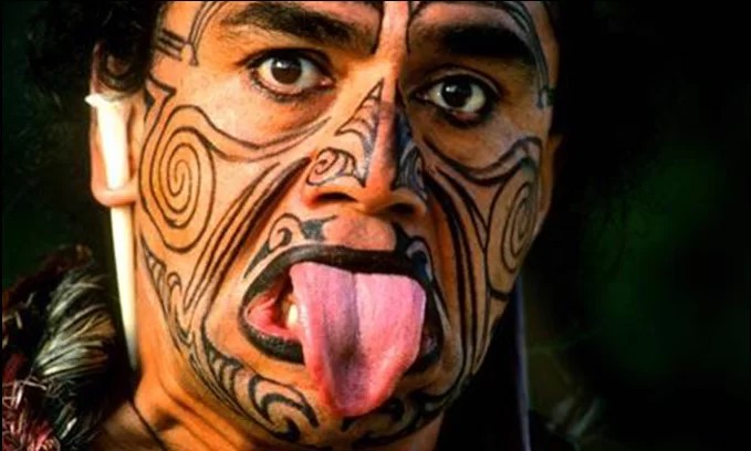 Maori warrior performing haka with ta moko facial tattoos, showing symbolic markings for cultural comparison