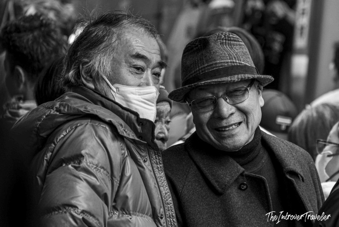 Two elderly Japanese men sharing a laugh at Tsukiji fish market, one wearing a face mask and puffer jacket