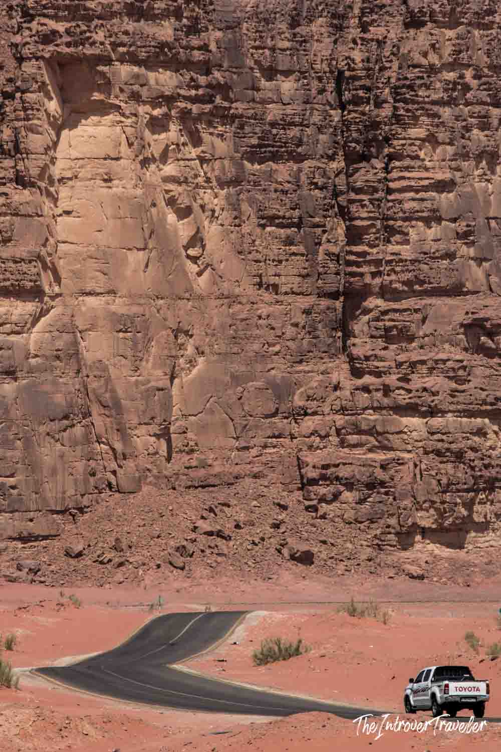 Winding road through Wadi Rum desert, Jordan, with a Toyota truck dwarfed by towering sandstone cliffs