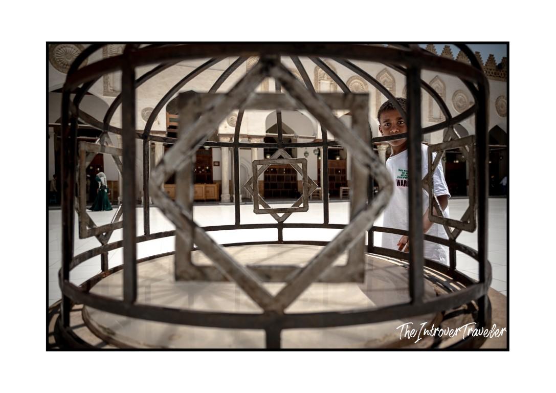 Boy peering through ornate iron geometric lattice in an Egyptian mosque courtyard