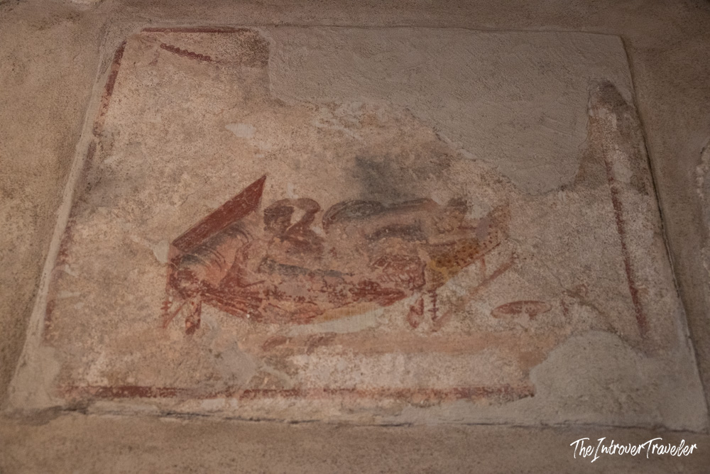 Faded erotic fresco on a stone wall inside the Lupanare brothel in Pompeii