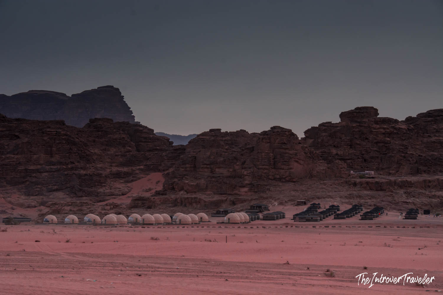Dome tent camp at dusk in Wadi Rum desert, Jordan, with red sand and sandstone cliffs