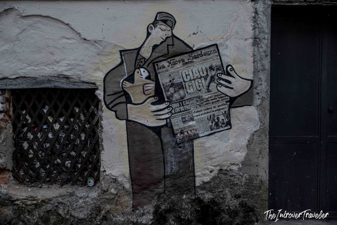 Street mural in Orgosolo showing a figure reading La Nuova Sardegna newspaper, Sardinia political art