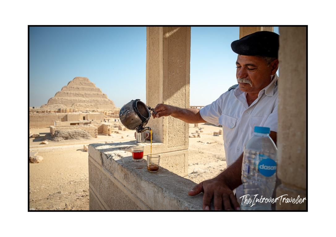 Egyptian man pouring tea with the Step Pyramid of Djoser at Saqqara in the background