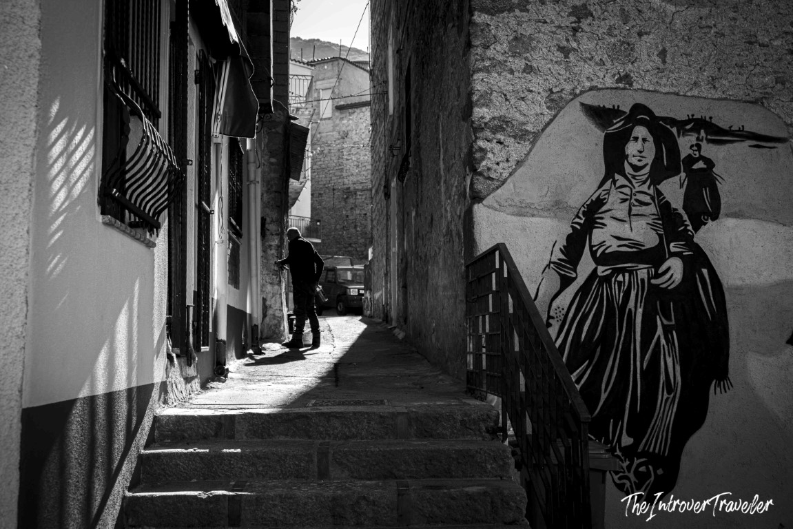 Street mural of a traditional Sardinian figure on a narrow alley wall in Orgosolo, Sardinia