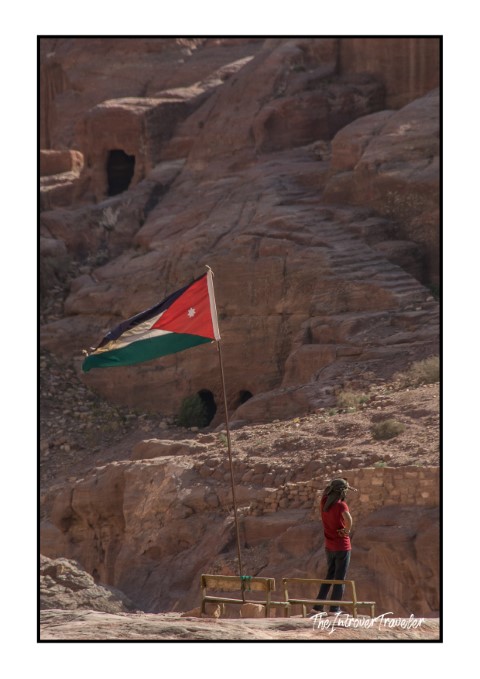 Traveler standing beside the Jordanian flag among the rose-red cliffs of Petra, Jordan