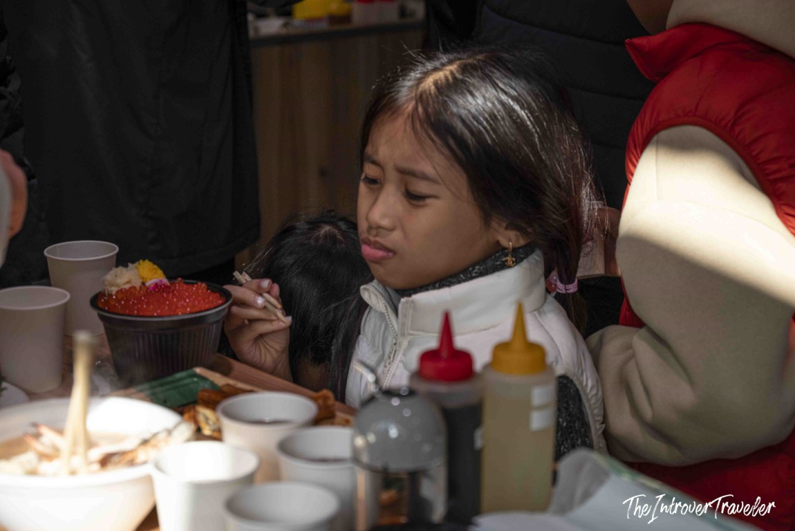 Girl eating ikura don (salmon roe rice bowl) with chopsticks at Tsukiji fish market, Tokyo
