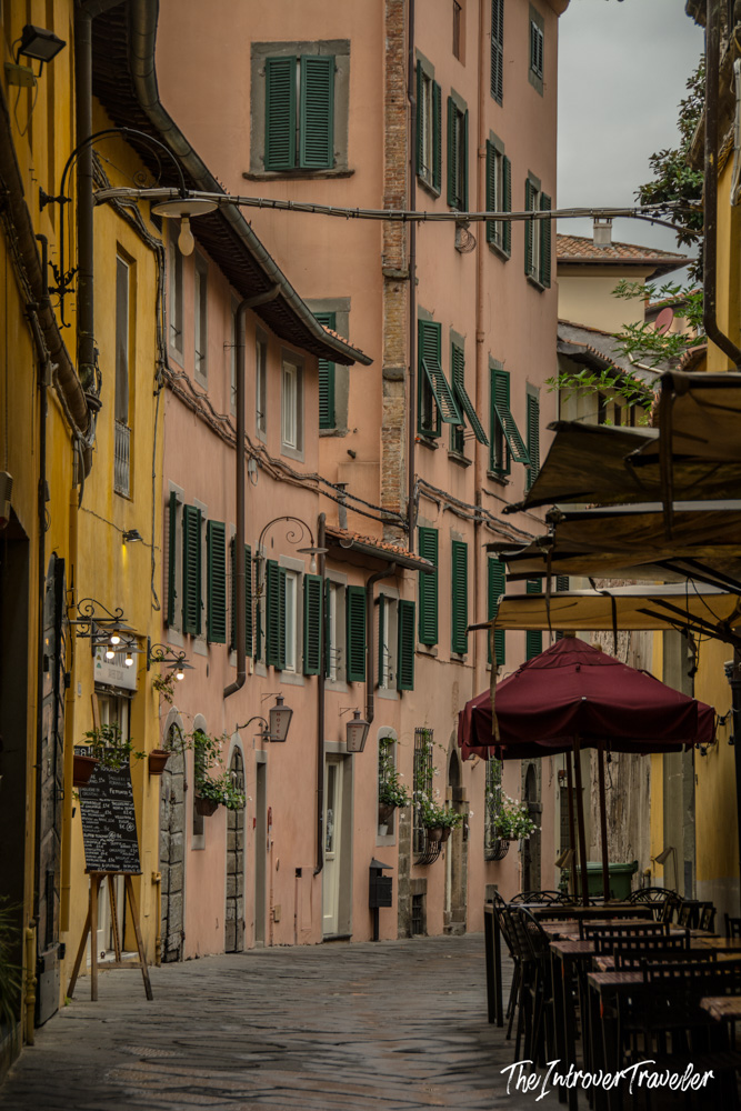 Narrow cobblestone street in Lucca's historic centre, lined with peach facades and green shutters