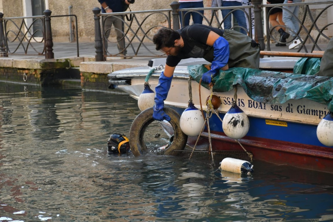 Diver and worker retrieving a tire from a Venice canal during an underwater cleanup operation