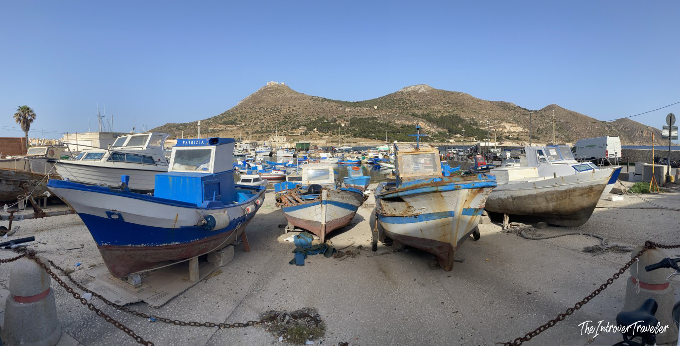 Weathered fishing boats dry-docked at Favignana harbor, with Monte Santa Caterina rising in the background