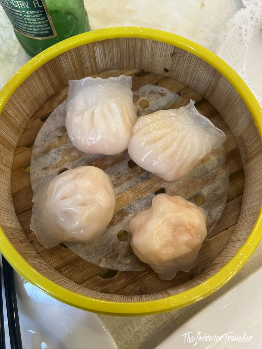 Four translucent har gow shrimp dumplings in a bamboo steamer at House of Joy, Chinatown Manhattan