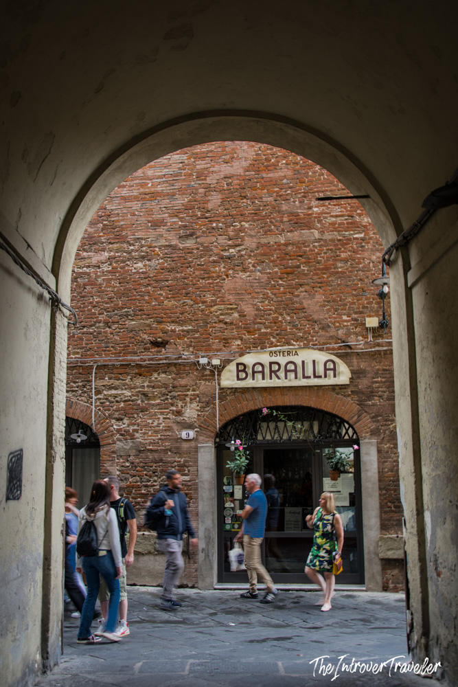 Osteria Baralla in Lucca, framed by a stone arch with pedestrians passing by