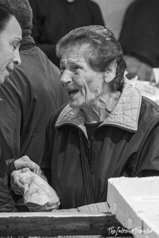 Elderly woman smiling and chatting at a bustling coastal city fish market stall