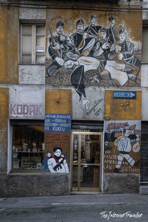 Political murals covering a building facade in Orgosolo, Sardinia, including Caccia Grossa a Orgosolo (1899)