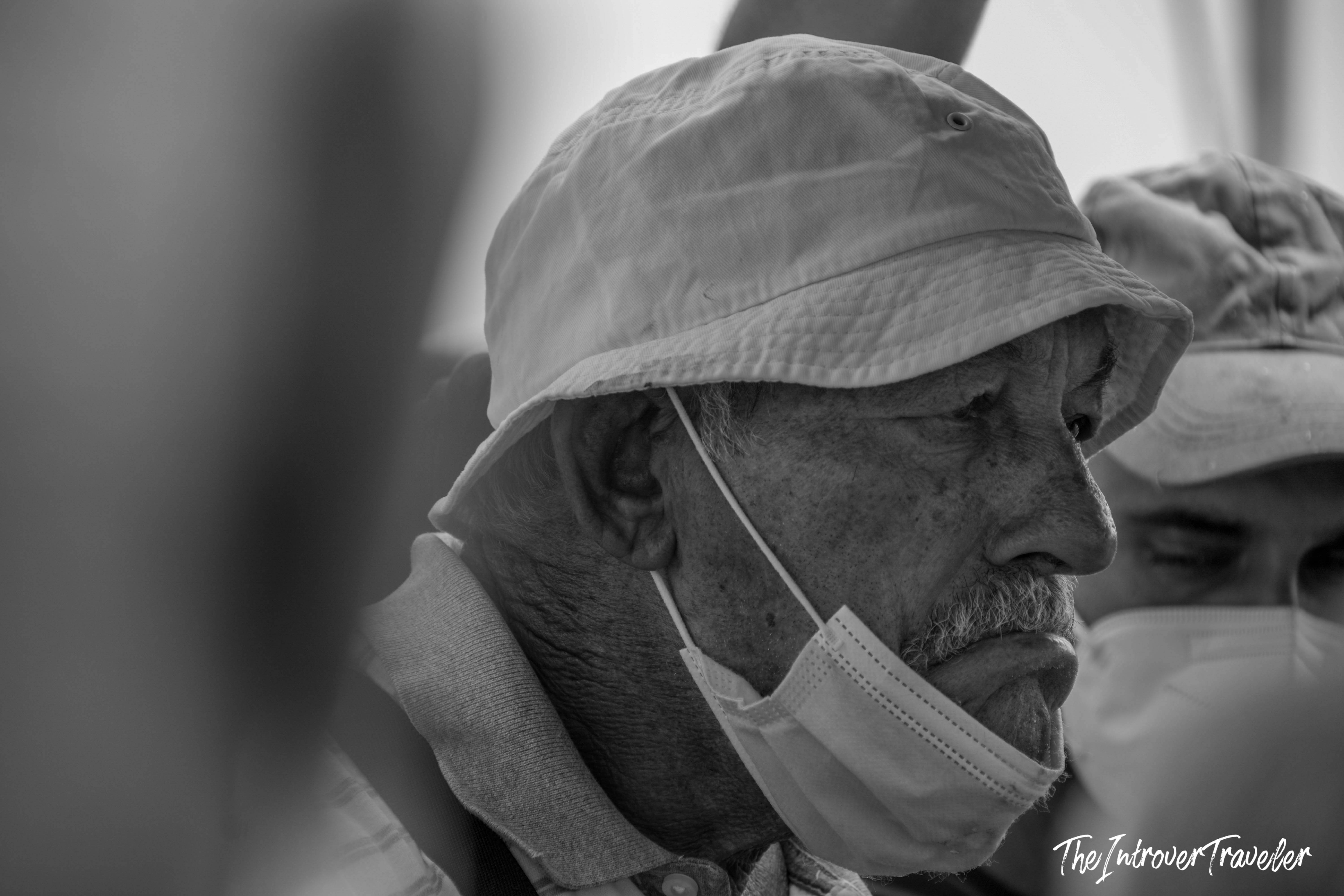 Elderly traveler with bucket hat and lowered face mask, captured candidly in Mazara del Vallo, Sicily
