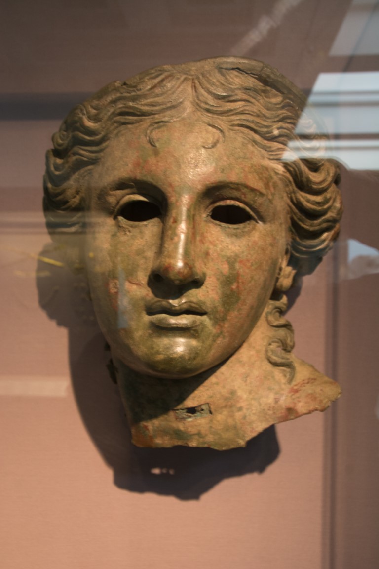 Ancient Greek or Roman bronze head fragment displayed in a glass case at the British Museum, London