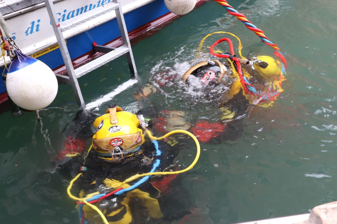 Venice canal divers in yellow helmets and dry suits surfacing beside a dive support boat