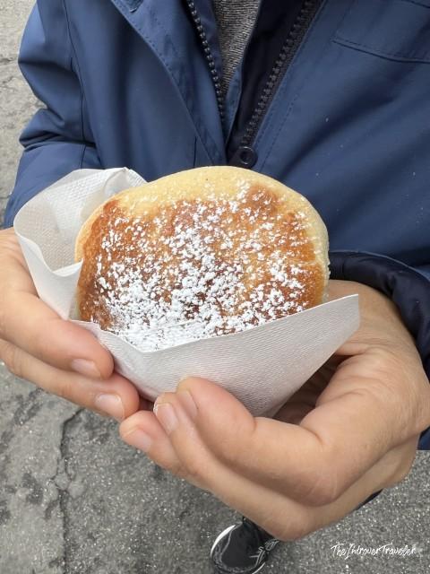 Hands holding a powdered sugar-dusted frolla sfogliatella wrapped in paper, Naples street food