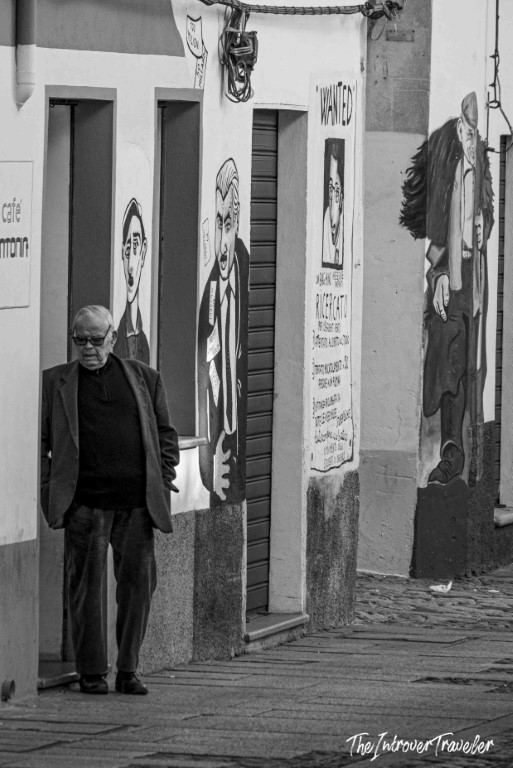 Elderly man standing beside political street murals in Orgosolo, Sardinia