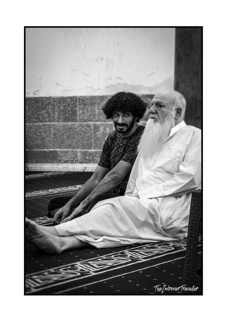 Two men resting on a prayer carpet in Egypt, young and elderly locals captured in candid street photography.