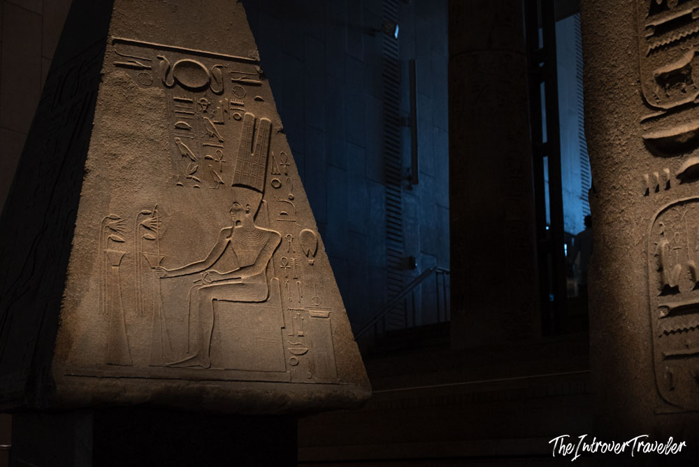 Ancient Egyptian obelisk relief with seated deity hieroglyphs, Grand Egyptian Museum staircase gallery