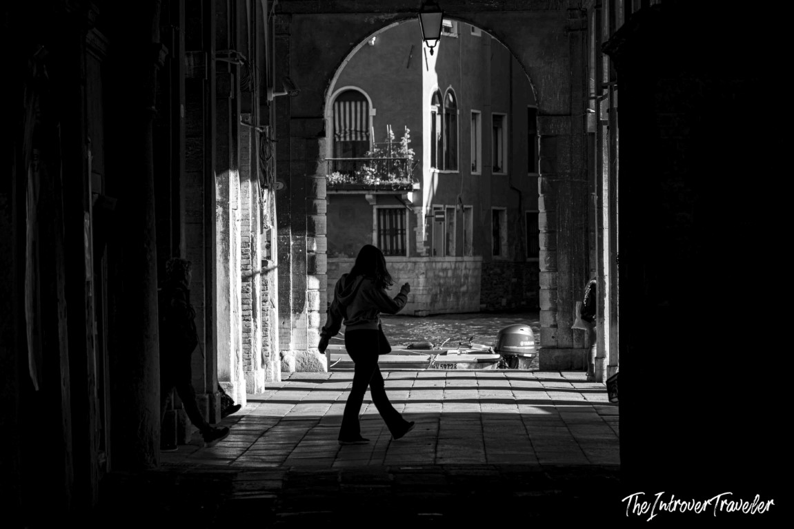 Woman silhouetted walking through a Venice canal archway toward a moored boat