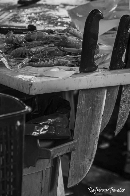 Fresh prawns and butcher knives on a vendor's table at a bustling coastal fish market