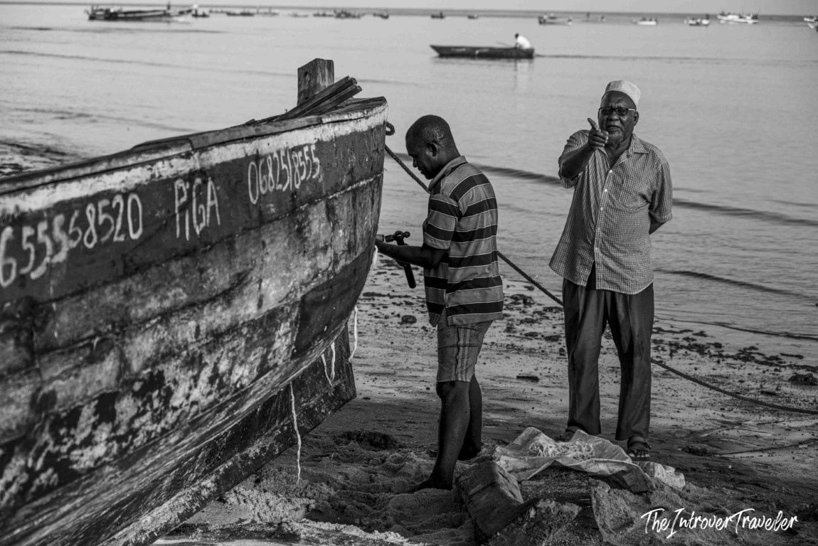 Two men repairing a traditional wooden fishing boat on a sandy East African coastal shore