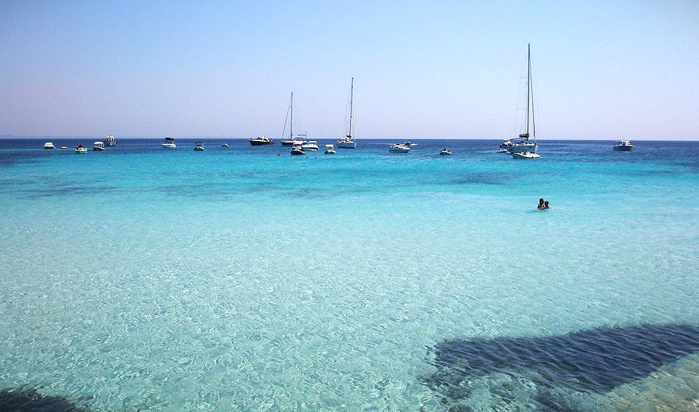 Crystal-clear turquoise waters of Cala Rossa, Favignana, with sailboats anchored offshore in the Egadi Islands