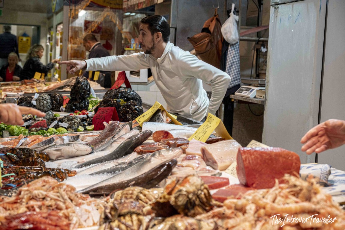 Vendor pointing at fresh fish, mussels, and tuna at a bustling coastal city fish market stall