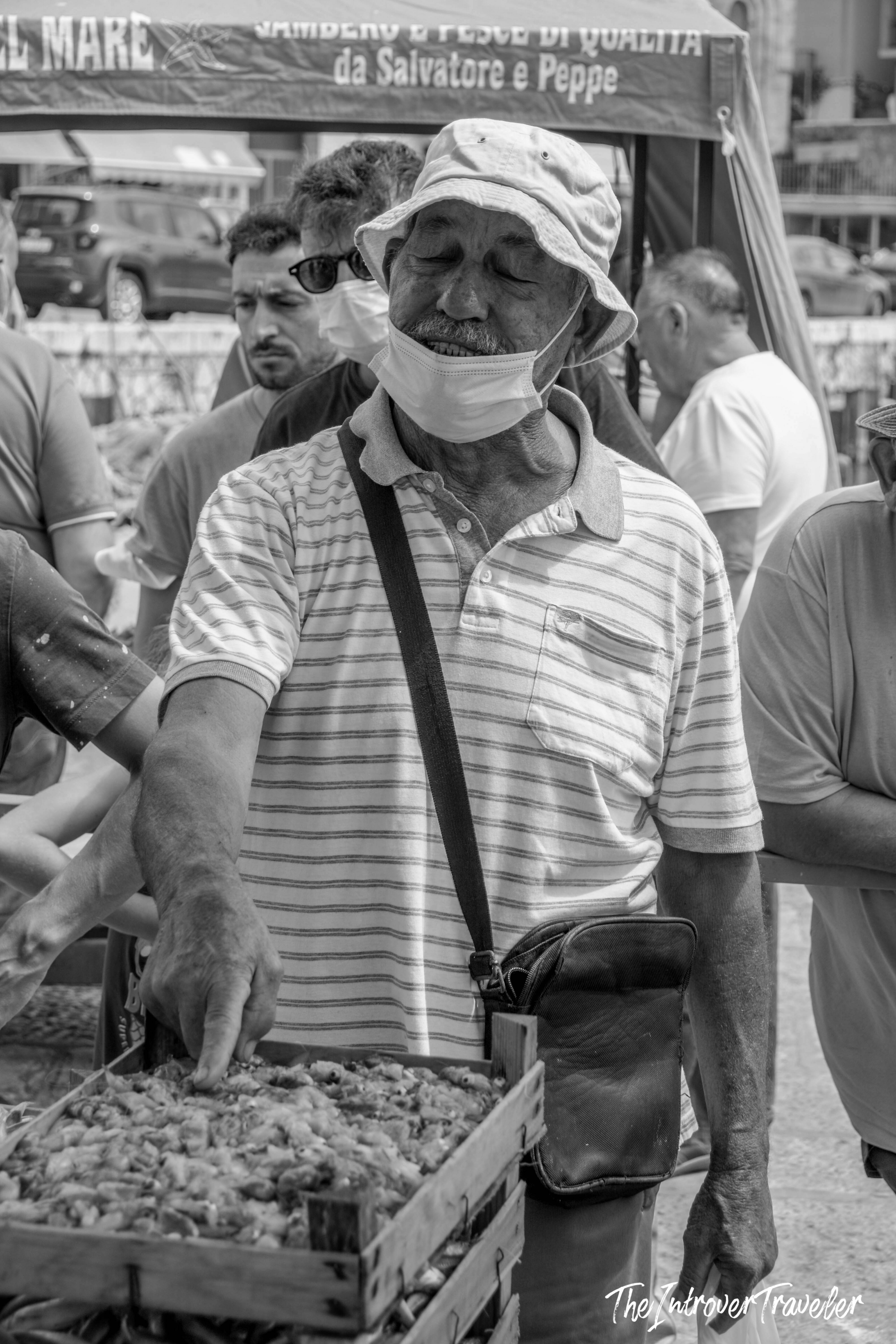 Smiling vendor selling seafood at a bustling outdoor market in Mazara del Vallo, Sicily