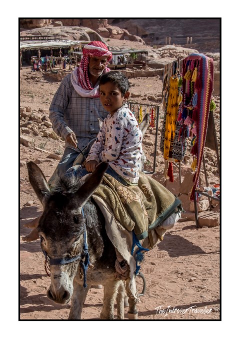 Bedouin man and child riding a donkey past souvenir stalls in Petra, Jordan