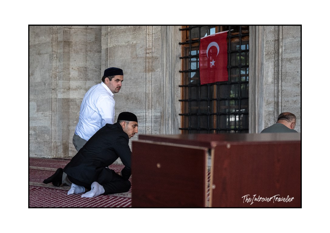 Muslim men praying on a carpet inside an Istanbul mosque, with a Turkish flag visible behind them