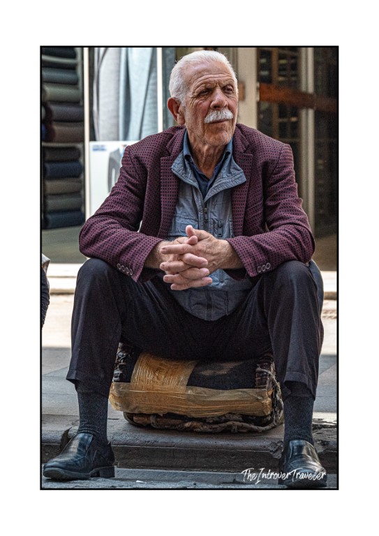 Elderly Turkish man resting on a wooden block outside a fabric shop in Istanbul