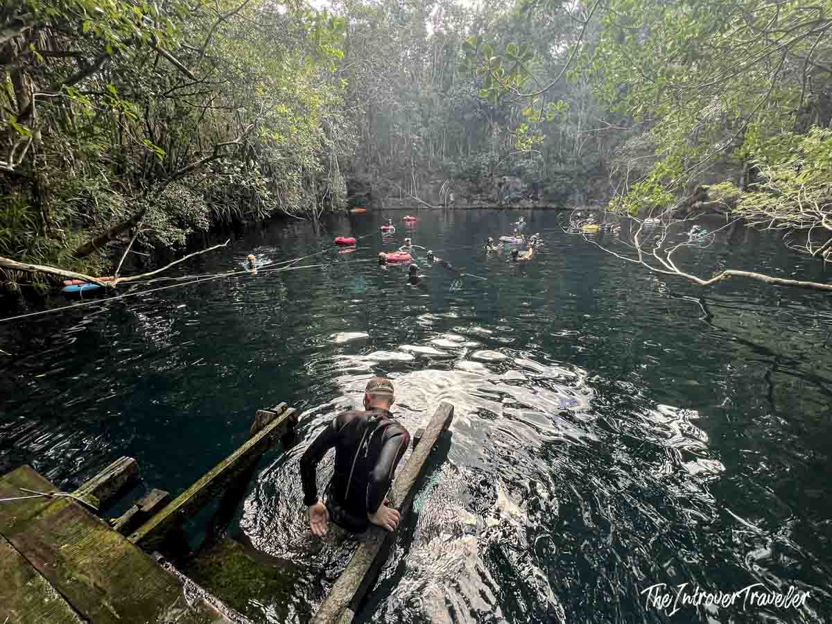 Diver in wetsuit entering the dark waters of Cenote Angelita, Yucatan, surrounded by dense jungle