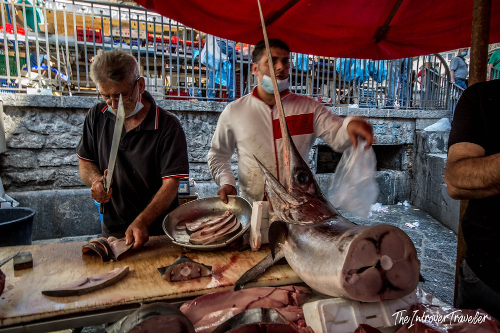 Vendors slicing fresh swordfish at a bustling coastal city fish market stall