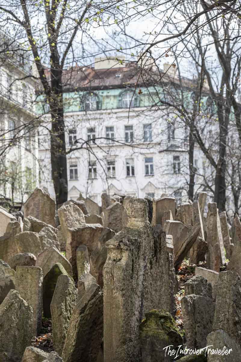 Crowded ancient headstones at the Old Jewish Cemetery in Prague, with city buildings beyond