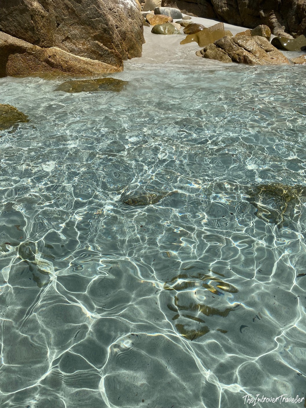 Crystal-clear shallow water lapping over sandy rocks at Porto Giunco beach, Villasimius, Sardinia