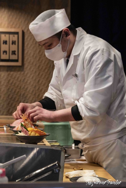 Japanese sushi chef carefully plating a fresh seafood donburi bowl at Tsukiji fish market Tokyo