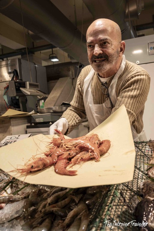 Friendly fishmonger at a coastal fish market proudly displaying fresh whole prawns on paper